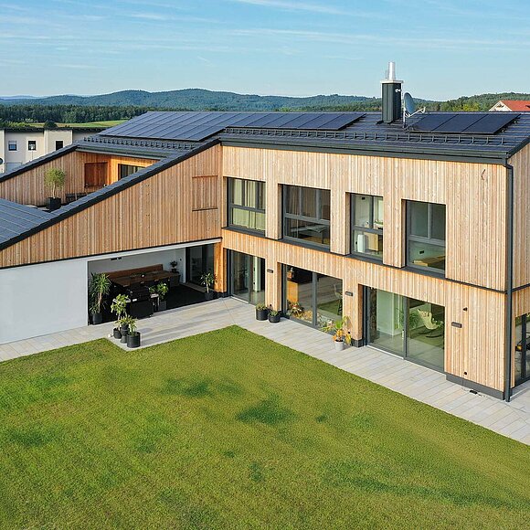 Zweigeschossiges modernes Wohnhaus mit Holzfassade und weißen Anbauelementen.