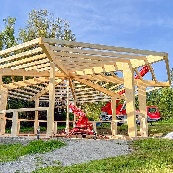 Holzkonstruktion eines offenen Unterstands im Aufbau auf einer grünen Baustelle.